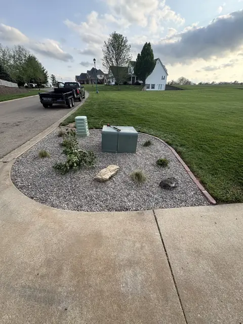 Completed corner bed with decorative rock, shrubs, accent stones, and edging around utility boxes